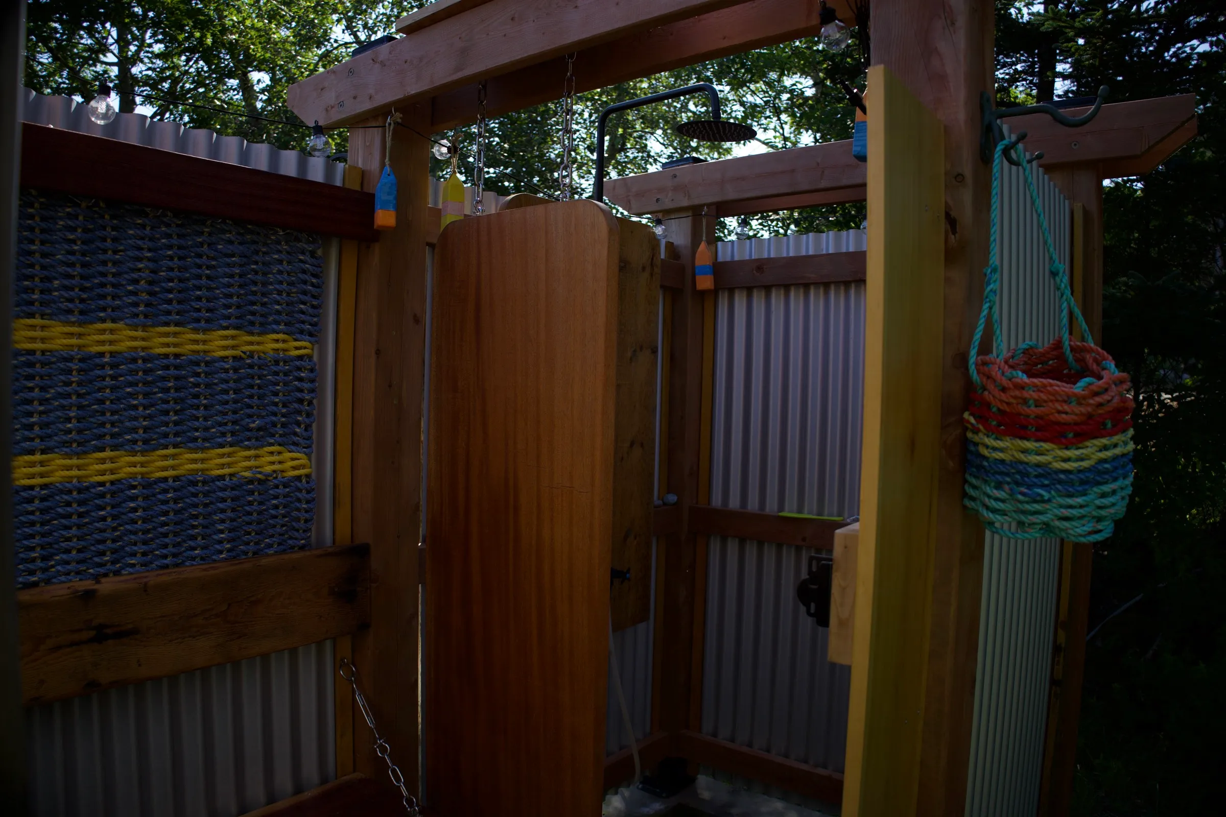 Inside the outdoor shower: rainfall head, cedar walls, string lights and lobster-rope art