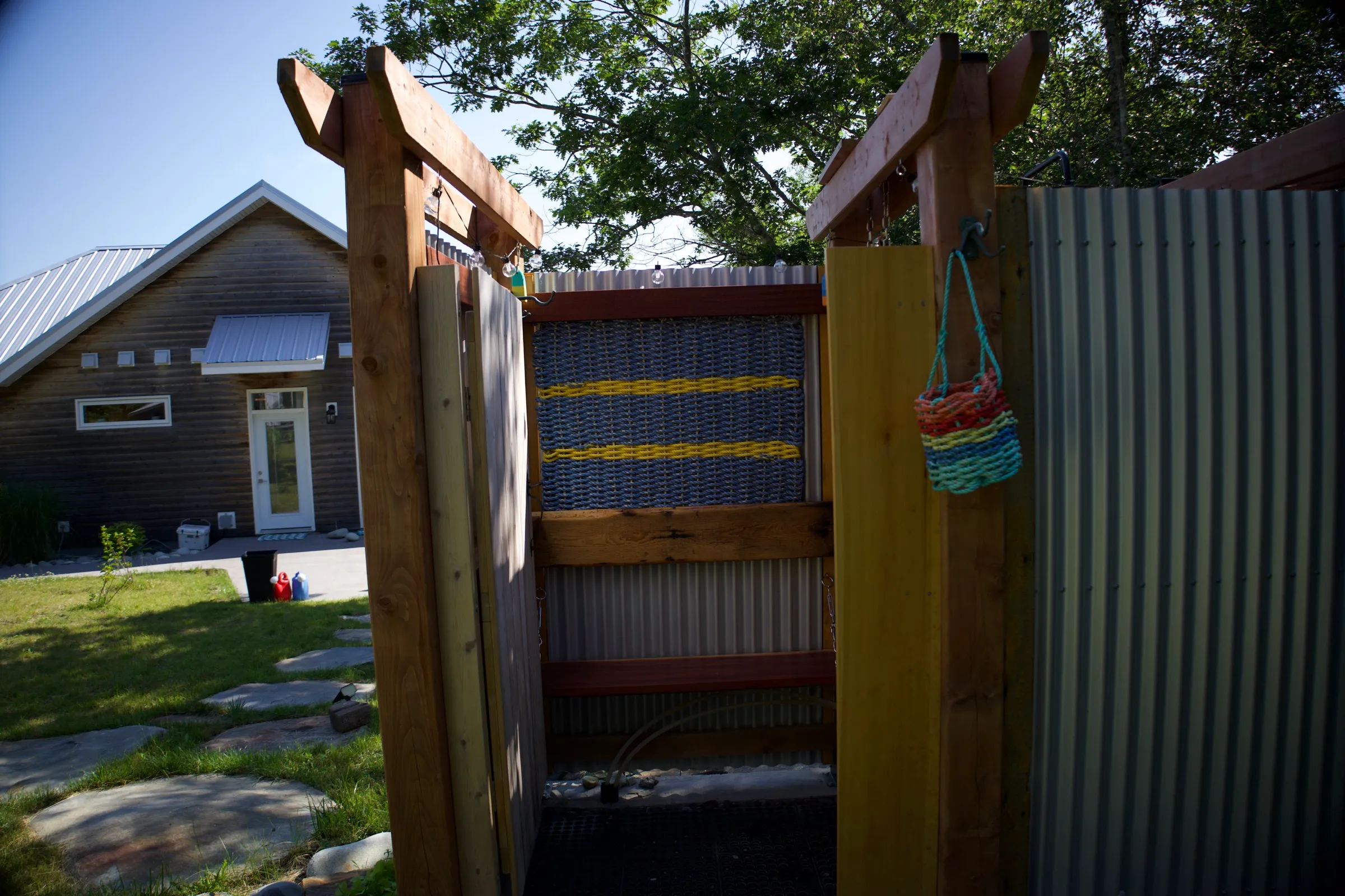 The outdoor shower's cedar bench and woven rope panel, with the cottage beyond the open door
